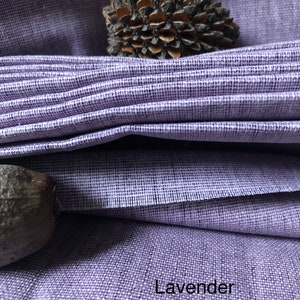 K&ouml;nnte beinhalten: Nahaufnahme eines lavendelfarbenen Stoffes mit einer strukturierten Webart. Der Stoff ist gefaltet und das Wort "Lavender" ist in der unteren rechten Ecke aufgedruckt.