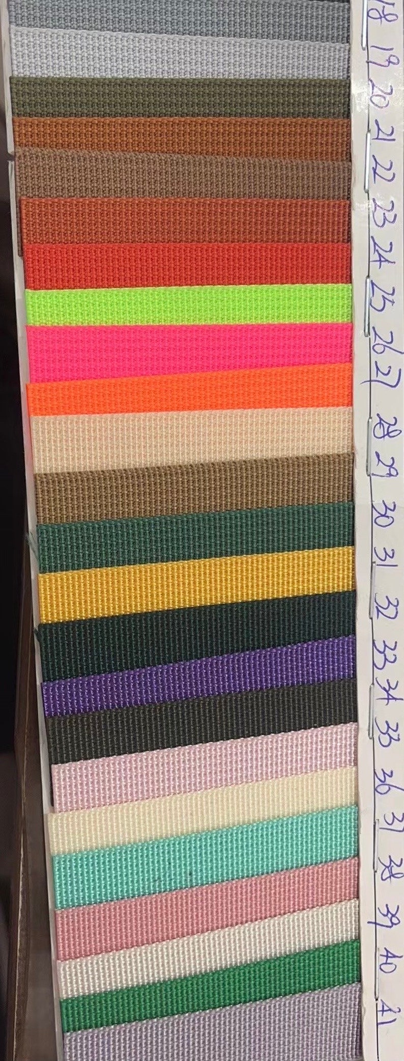 May include: A sample card of 24 different colors of woven webbing. The colors range from light gray to dark purple. The card is labeled with numbers 18 through 41.