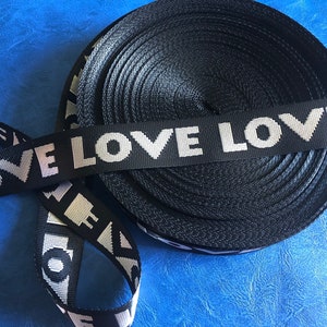 May include: Black and white woven ribbon with the words "LOVE LOVE" repeated. The ribbon is rolled up and the ends are visible.