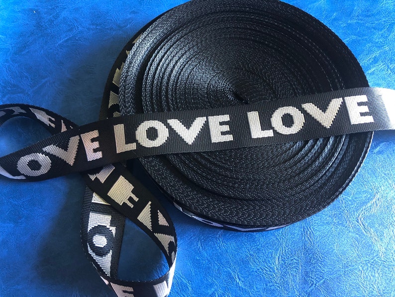 May include: Black and white woven ribbon with the words "LOVE LOVE" repeated. The ribbon is rolled up and the ends are visible.