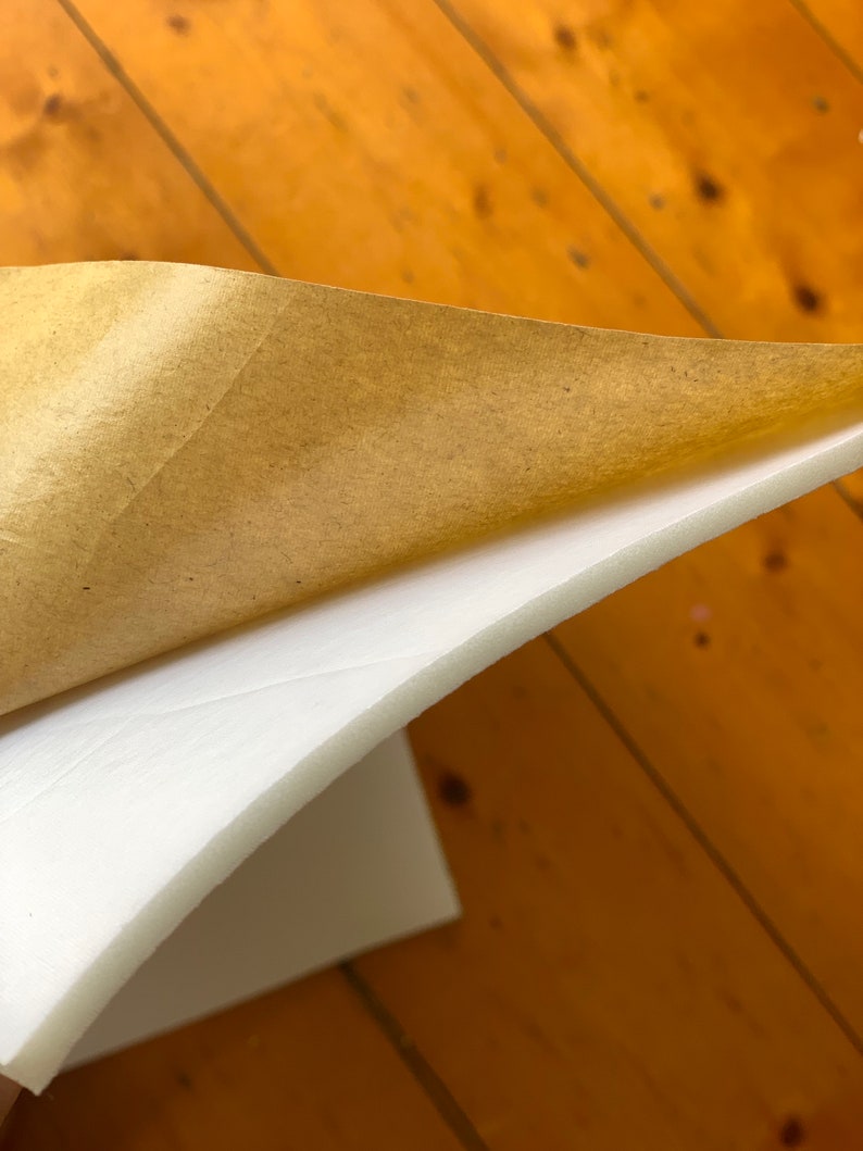 Puede incluir: Una l&aacute;mina de espuma blanca con un respaldo de papel marr&oacute;n. El papel est&aacute; parcialmente despegado para revelar la espuma.