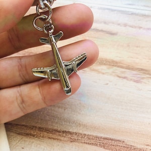 May include: Silver airplane keyring with a detailed design. The keyring is attached to a silver chain.