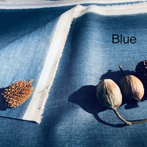K&ouml;nnte beinhalten: Nahaufnahme eines blauen Stoffes mit wei&szlig;em Rand. Der Stoff ist in der Mitte gefaltet und es liegen drei braune Samenkapseln und ein Tannenzapfen auf dem Stoff. Der Text "Blue" ist auf dem Stoff geschrieben.