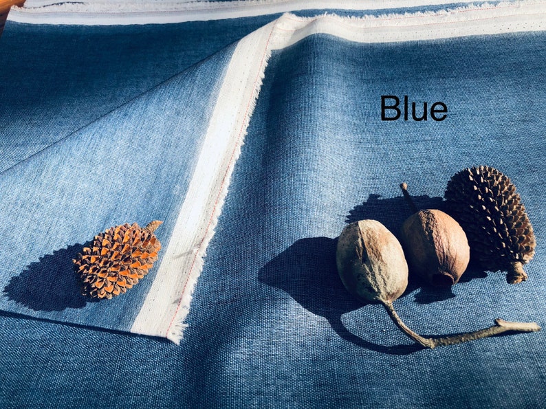 K&ouml;nnte beinhalten: Nahaufnahme eines blauen Stoffes mit wei&szlig;em Rand. Der Stoff ist in der Mitte gefaltet und es liegen drei braune Samenkapseln und ein Tannenzapfen auf dem Stoff. Der Text "Blue" ist auf dem Stoff geschrieben.