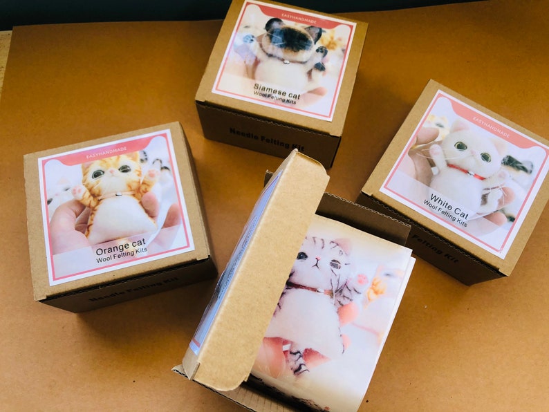 May include: Four boxes containing wool felting kits for making different colored cats. The boxes are brown with white labels and feature images of the finished felted cats. The labels include the text "Orange cat", "Siamese cat", "White Cat", and "Wool Felting Kits".