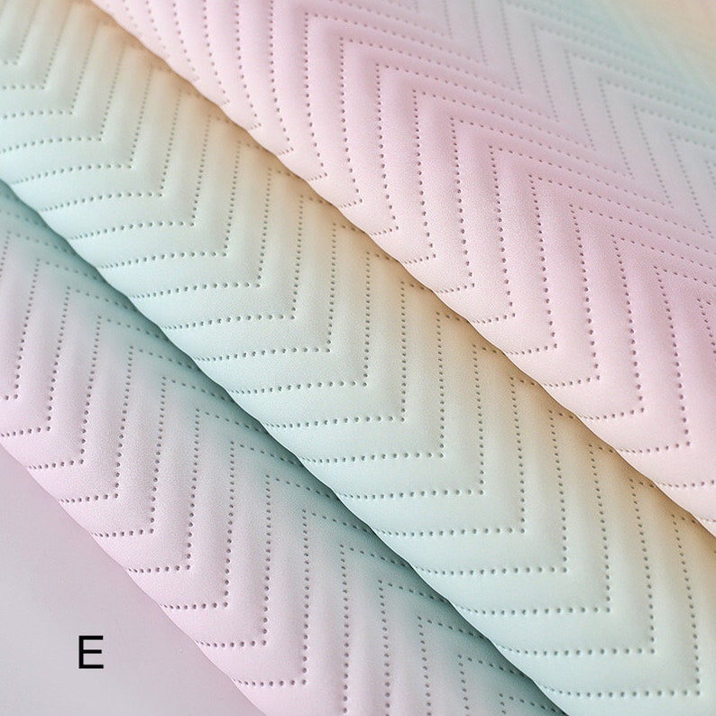 May include: Two pieces of fabric with a chevron pattern in a gradient of pastel colors, including pink, blue, and yellow. The fabric has a quilted texture with small dots.