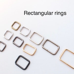May include: Assortment of rectangular metal rings in various sizes and finishes, including gold, silver, and black.  Rectangular rings.