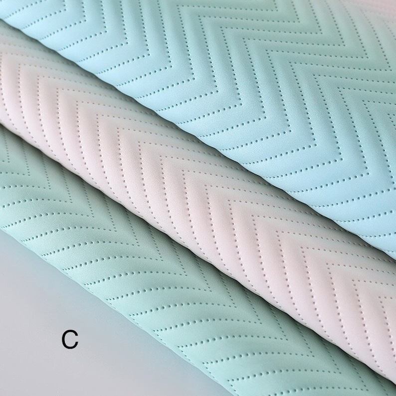 May include: Three pieces of fabric with a chevron pattern. The fabric is a light blue, a light green, and a light pink. The fabric has a textured surface with small dots.