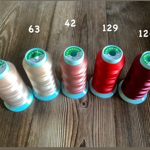 May include: Six spools of thread in various colors, including beige, light pink, red, and burgundy. The spools are labeled with numbers, including 40, 63, 42, 129, and 126.