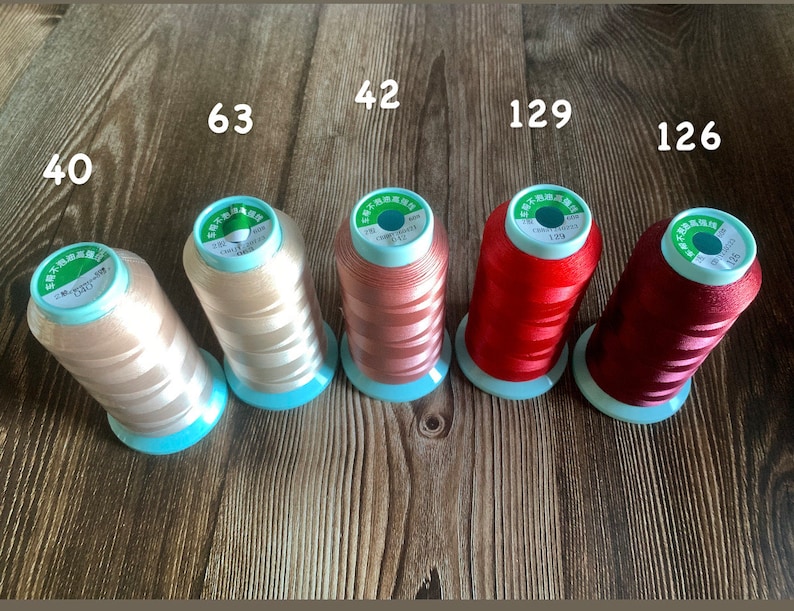 May include: Six spools of thread in various colors, including beige, light pink, red, and burgundy. The spools are labeled with numbers, including 40, 63, 42, 129, and 126.