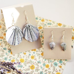 Può includere: Due paia di orecchini pendenti su cartoncini beige. La coppia più grande presenta cerchi in carta plissettata azzurra con pois blu scuro. La coppia più piccola è composta da forme in carta piegata multicolore. Tutti hanno ganci argentati.