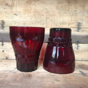 May include: Two vintage ruby red glass tumblers with a textured design. The tumblers are on a wooden surface.