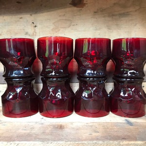 Puede incluir: Conjunto de cuatro vasos de vidrio rojo con un diseño texturizado y facetado. Los vasos están dispuestos en una fila sobre una superficie de madera.