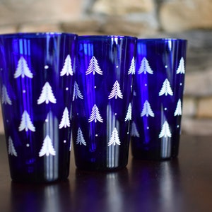 May include: Three cobalt blue glass tumblers with a white Christmas tree pattern.