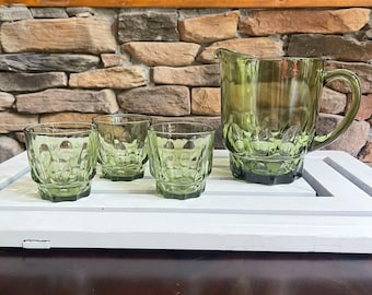 May include: A set of four green glass drinking glasses and a matching pitcher. The glasses and pitcher have a textured, dimpled design.