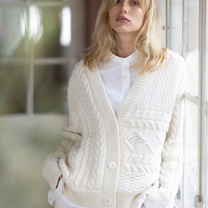 Könnte beinhalten: Ein weißer Strickcardigan mit V-Ausschnitt und Knopfleiste. Der Cardigan hat ein strukturiertes Muster und wird über einem weißen Hemd mit Kragen getragen.