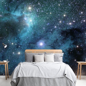 May include: A bedroom with a cosmic theme. The wall behind the bed features a vibrant mural of a nebula with stars in shades of blue, teal, and purple. A wooden bed frame is paired with gray bedding and white pillows. Two small wooden side tables flank the bed.