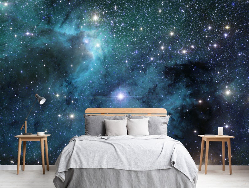May include: A bedroom with a cosmic theme. The wall behind the bed features a vibrant mural of a nebula with stars in shades of blue, teal, and purple. A wooden bed frame is paired with gray bedding and white pillows. Two small wooden side tables flank the bed.