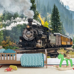 May include: A wooden toddler bed with a teal chevron blanket and polka dot pillows, positioned in front of a wall mural depicting a black steam locomotive numbered 482 on a bridge. A green wooden rocking moose and two small toy cars are on the floor.