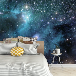 May include: A bedroom with a galaxy-themed wall mural. The bed has a gray and white striped comforter and pillows. A yellow wall and a small side table with a plant and clock complete the scene.