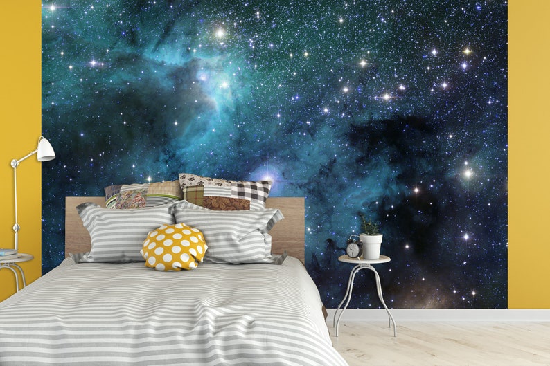 May include: A bedroom with a galaxy-themed wall mural. The bed has a gray and white striped comforter and pillows. A yellow wall and a small side table with a plant and clock complete the scene.