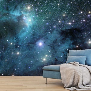 May include: A wall mural depicting a vibrant nebula in shades of teal and blue, speckled with numerous bright stars. A teal sofa with pillows and a beige blanket is placed in front of the mural, creating a cozy atmosphere.