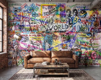 Könnte beinhalten: Ein braunes Ledersofa steht vor einer Wand mit buntem Graffiti, das verschiedene Sätze wie Free World, Be Human und Dream Believe sowie Illustrationen von Augen, Gesichtern und einer Flagge zeigt, mit einem hölzernen Couchtisch davor.