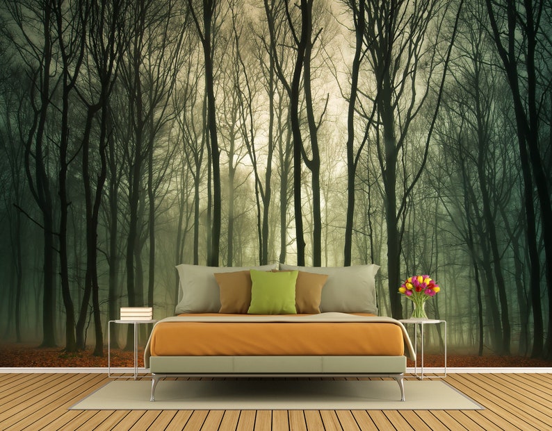 May include: A bedroom interior design with a bed featuring a light orange comforter and a forest scene wallpaper. The wallpaper depicts a misty forest with tall trees and a light green background. The bed has a white headboard and two side tables with lamps. There are flowers in a vase on one of the tables.