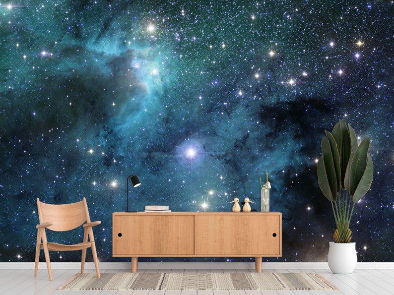 May include: A room featuring a vibrant space-themed wall mural with a wooden cabinet, chair, and potted plant. The mural depicts a nebula with stars in shades of blue and teal. A black desk lamp and decorative items are on the cabinet.