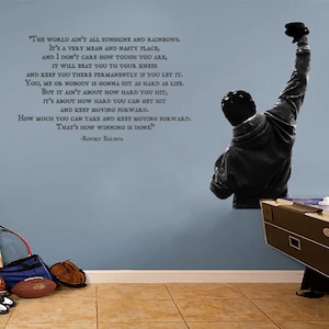 May include: A black and white wall decal of a man with his fist raised in the air. The decal is accompanied by a motivational quote from the movie Rocky Balboa: "The world ain't all sunshine and rainbows. It's a very mean and nasty place, and I don't care how tough you are, it will beat you to your knees and keep you there permanently if you let it. You, me or nobody is gonna hit as hard as life. But it ain't about how hard you hit, it's about how hard you can get hit and keep moving forward. How much you can take and keep moving forward. That's how winning is done!" -Rocky Balboa