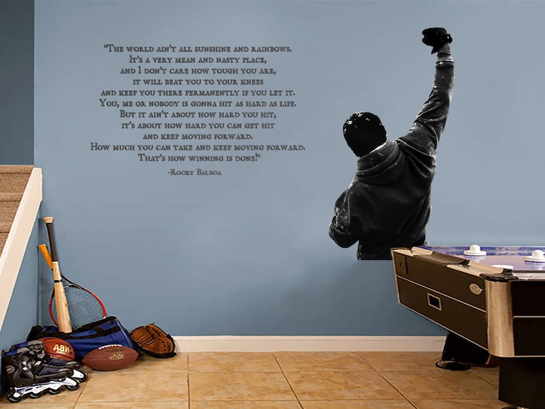 May include: A black and white wall decal of a man with his fist raised in the air. The decal is accompanied by a motivational quote from the movie Rocky Balboa: "The world ain't all sunshine and rainbows. It's a very mean and nasty place, and I don't care how tough you are, it will beat you to your knees and keep you there permanently if you let it. You, me or nobody is gonna hit as hard as life. But it ain't about how hard you hit, it's about how hard you can get hit and keep moving forward. How much you can take and keep moving forward. That's how winning is done!" -Rocky Balboa
