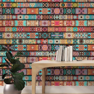 Op de afbeelding: Een kleurrijke muur met een herhalend patroon van rechthoekige tegels in tinten van teal, oranje, bruin en paars. Een houten tafel met boeken en een plant in een zilveren pot staat voor de muur.