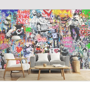 Op de afbeelding: Een grote muurschildering met een levendige graffiti-stijl collage met kleurrijke verfspatten, stripfiguren zoals Mickey en Minnie Mouse, een robot en tekst waaronder "ALWAYS DREAM BIG" en "never never over up" op een witte muur.