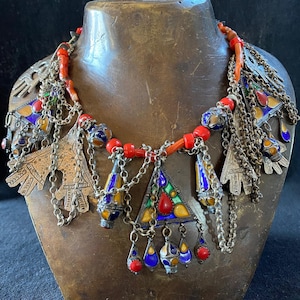 Può includere: Una collana in argento e corallo con disegni smaltati e geometrici. La collana presenta più ciondoli, tra cui un grande ciondolo triangolare con smalto rosso, verde, blu e giallo.