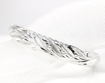 May include: A silver ring with a detailed leaf and bead design. The ring is set against a white background, highlighting the intricate patterns and the ring's polished finish. The ring's design features a series of leaves and small beads.
