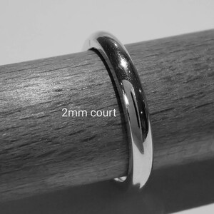 Puede incluir: Primer plano de una alianza de boda de 2 mm de ancho, un dise&ntilde;o simple y elegante, mostrada sobre una superficie de madera.