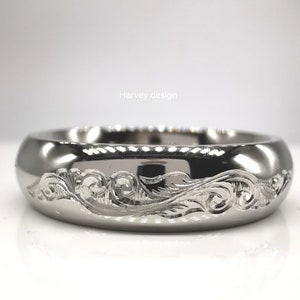 May include: A silver band with an intricate engraved design. The design features a wave-like pattern with swirls and leaves.