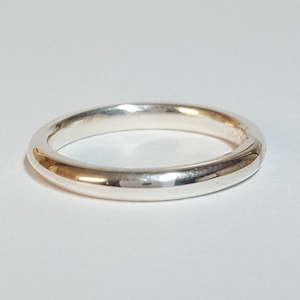 Puede incluir: Un anillo de banda de plata simple con una superficie lisa y redondeada.