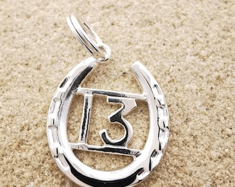 May include: Silver horseshoe charm with the number 13 inside. The horseshoe has a textured design.