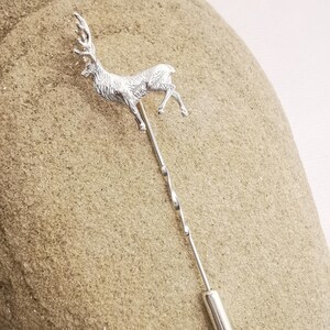 May include: A silver deer lapel pin with a twisted pin and a silver cap on the end.