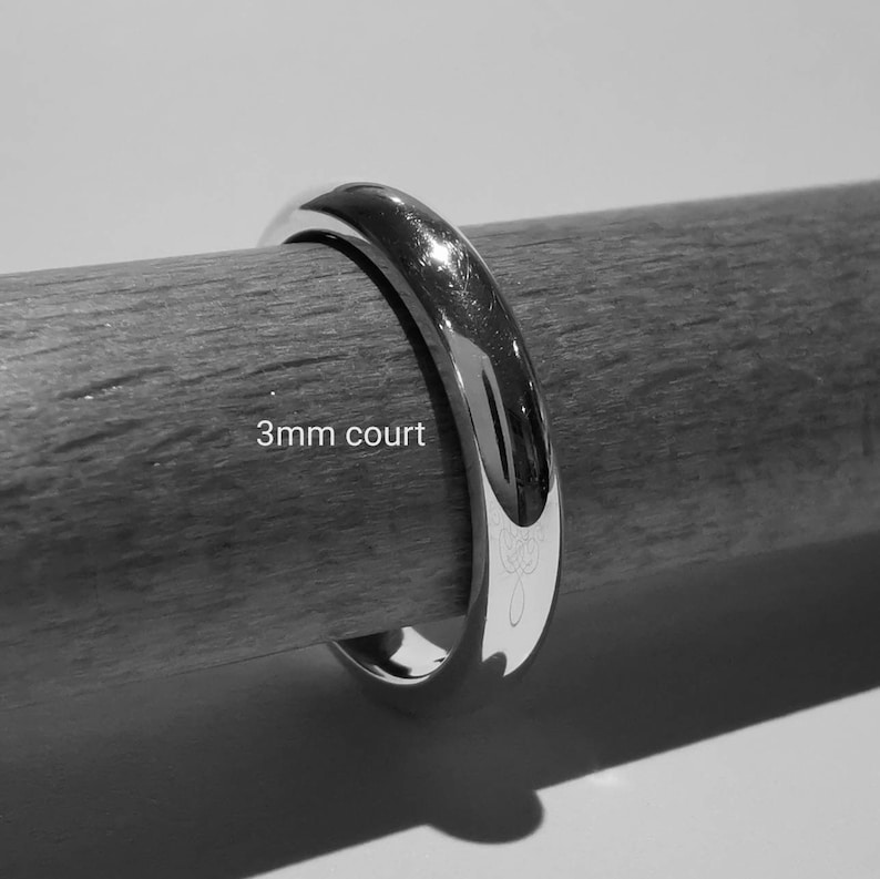 Puede incluir: Una alianza de boda de plata de 3 mm de ancho sobre una superficie de madera.