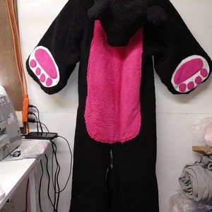 May include: Black and pink fleece hooded jumpsuit with paw print details on the sleeves and back.