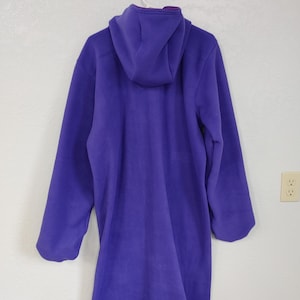 May include: A long purple fleece robe with a hood. The robe is hanging on a hook.