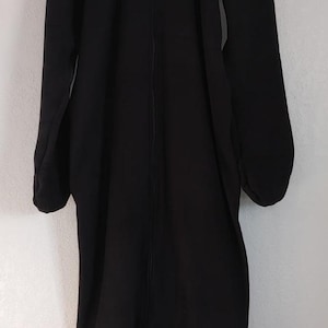 Op de afbeelding: Een lange zwarte gekapte robe met een ritssluiting. De robe heeft een kleine metalen hartvormige rits.