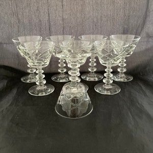 May include: Set of eight clear glass stemmed cocktail glasses with a diamond pattern. The glasses are arranged in a circle on a black surface.
