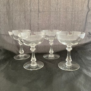 May include: Set of four clear glass champagne coupes with a fluted design. The coupes are arranged in a square formation on a black surface.