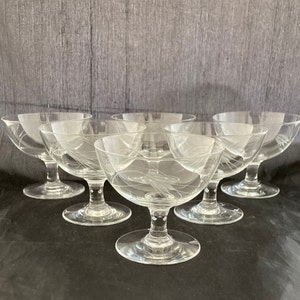 May include: Set of six clear glass dessert dishes with a delicate etched design. The dishes have a wide bowl and a short stem.