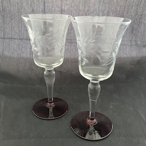 May include: Two clear glass wine glasses with etched floral designs and burgundy colored bases.