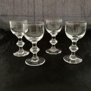 May include: Set of four clear glass stemmed shot glasses with a decorative design on the stem.
