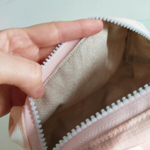 May include: A pink zippered pouch with a white zipper and a light beige fabric lining.